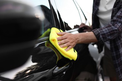 Photo of Man wiping car with yellow microfiber rag, closeup
