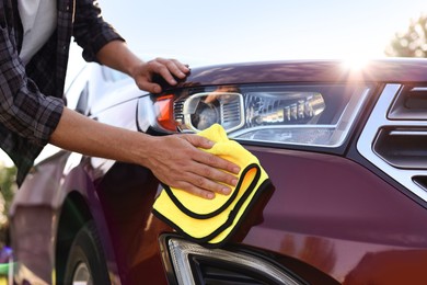 Photo of Man wiping car with yellow microfiber rag outdoors, closeup