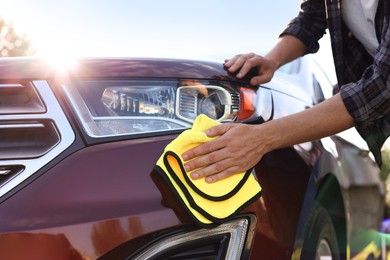 Photo of Man wiping car with yellow microfiber rag outdoors, closeup