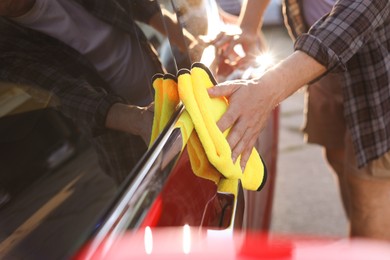 Photo of Man wiping car with yellow microfiber rag outdoors, closeup