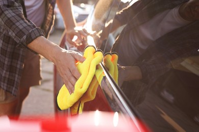 Photo of Man wiping car with yellow microfiber rag outdoors, closeup