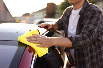 Photo of Man wiping car with yellow microfiber rag outdoors, closeup