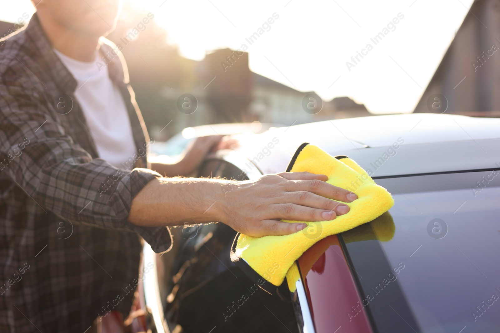 Photo of Man wiping car with yellow microfiber rag outdoors, closeup