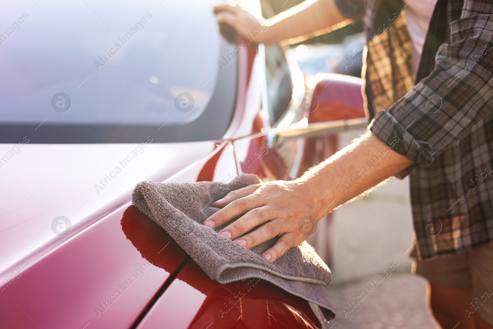 Photo of Man wiping car with grey microfiber rag outdoors, closeup