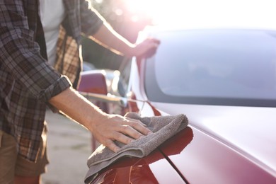 Photo of Man wiping car with grey microfiber rag outdoors, closeup