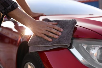 Photo of Man wiping car with grey microfiber rag outdoors, closeup