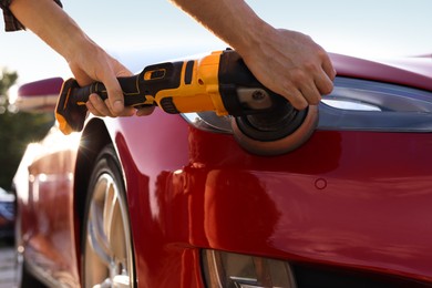 Photo of Man polishing car headlight with orbital polisher outdoors, closeup