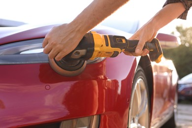 Photo of Man polishing car headlight with orbital polisher outdoors, closeup
