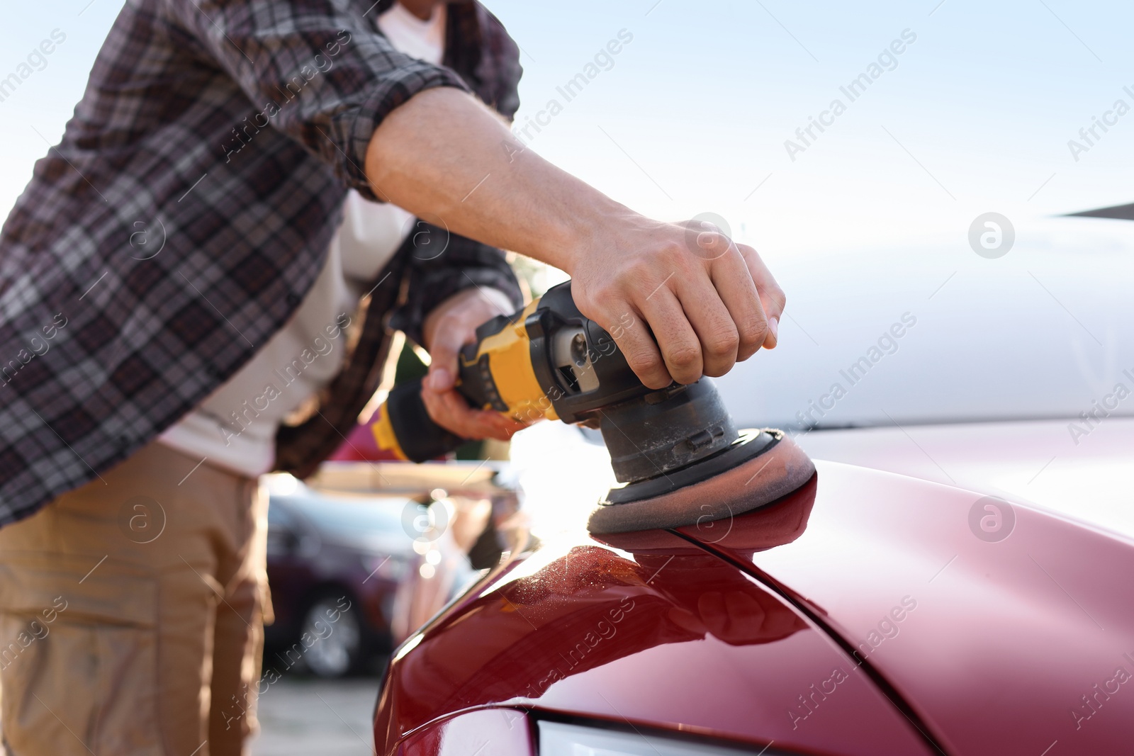Photo of Man polishing car hood with orbital polisher outdoors, closeup
