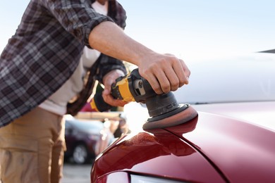 Photo of Man polishing car hood with orbital polisher outdoors, closeup