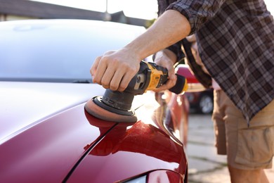 Photo of Man polishing car hood with orbital polisher outdoors, closeup