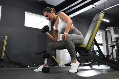 Photo of Athletic woman training with dumbbell on exercise bench in gym, low angle view