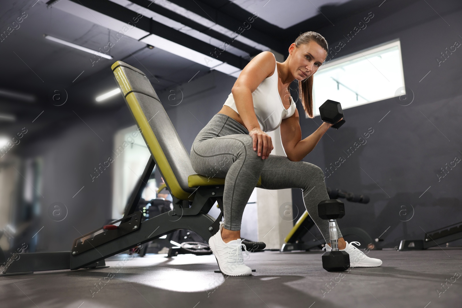 Photo of Athletic woman training with dumbbell on exercise bench in gym, low angle view