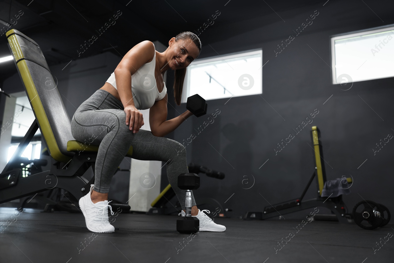 Photo of Athletic woman training with dumbbell on exercise bench in gym, low angle view. Space for text