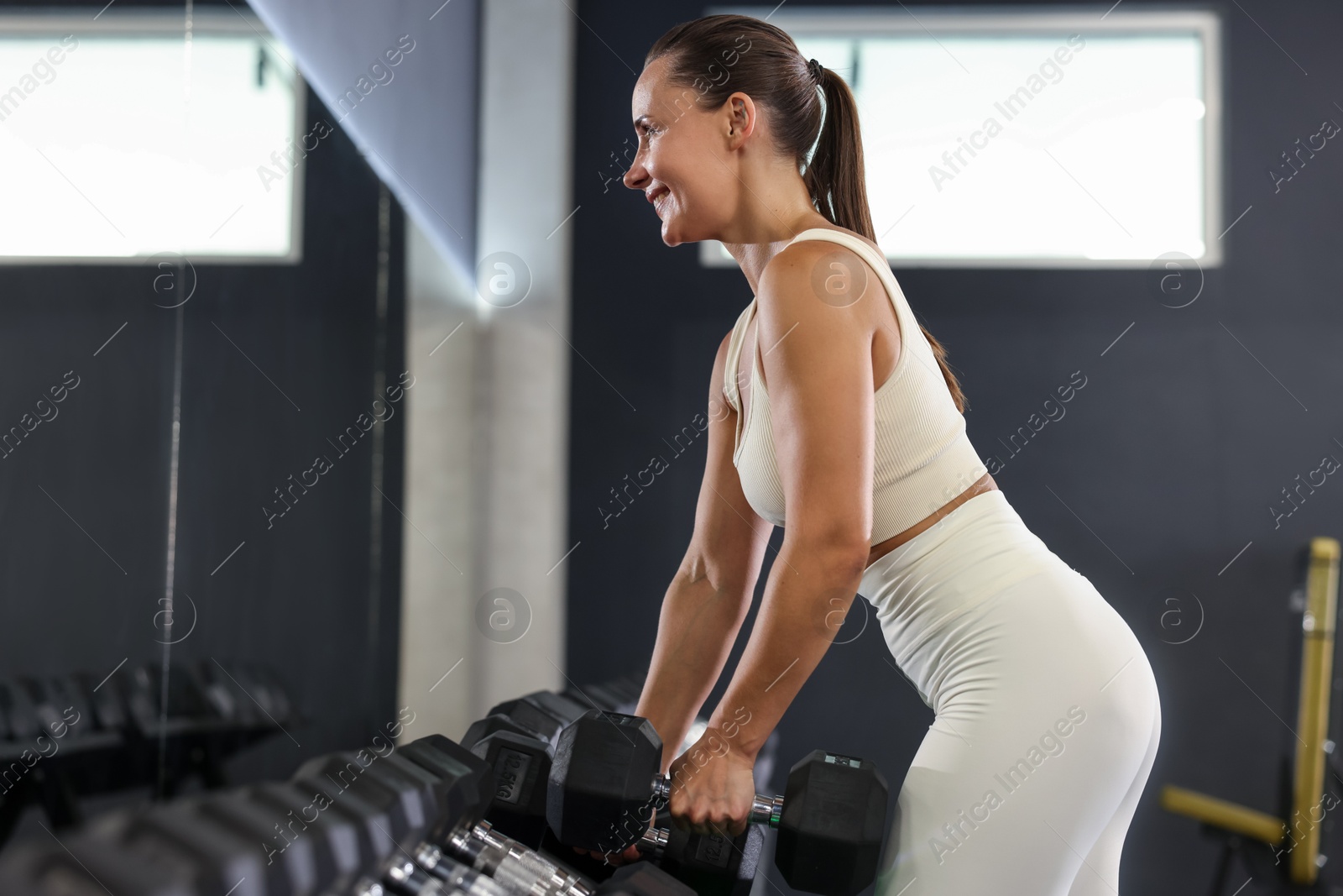 Photo of Smiling woman taking dumbbell near mirror in gym