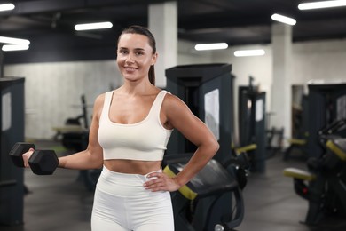 Photo of Smiling woman training with dumbbell in gym. Space for text