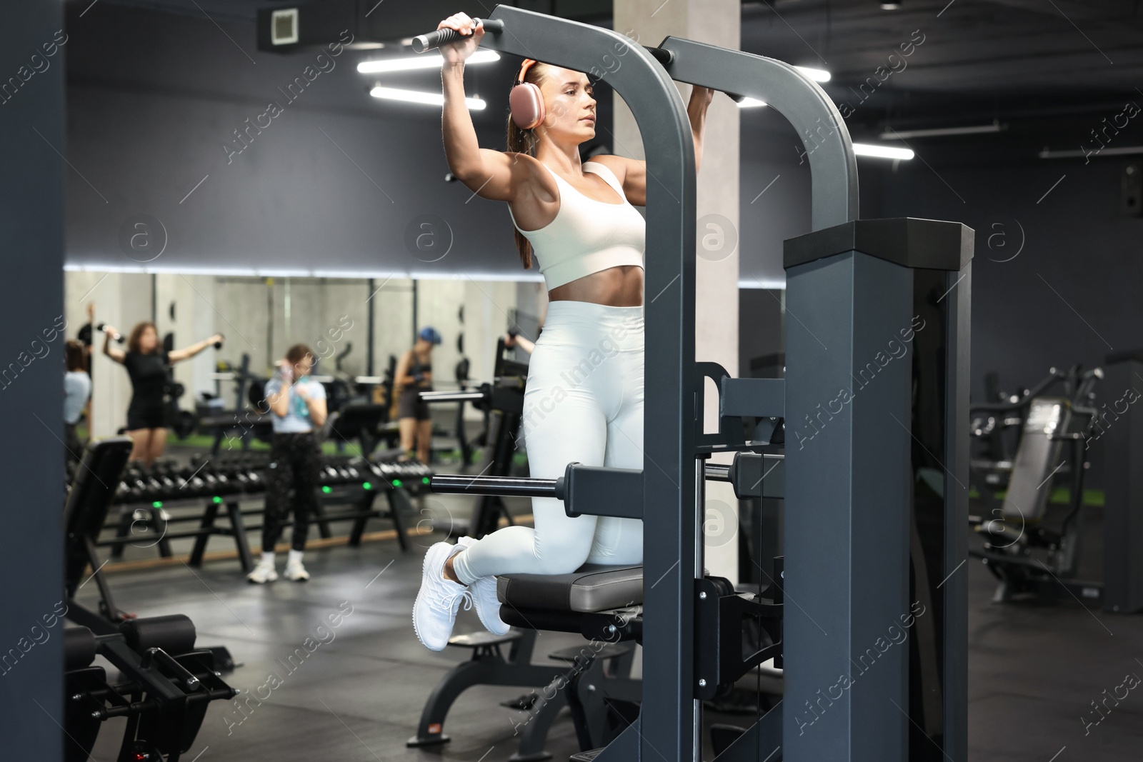Photo of Athletic woman in headphones training on pull up machine in gym
