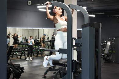 Photo of Athletic woman in headphones training on pull up machine in gym