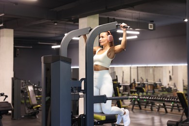 Photo of Athletic woman in headphones training on pull up machine in gym