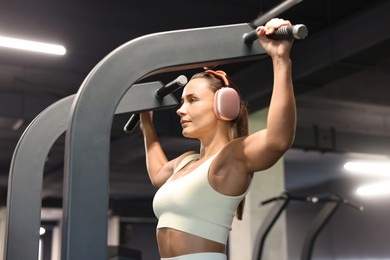 Photo of Athletic woman in headphones training on pull up machine in gym