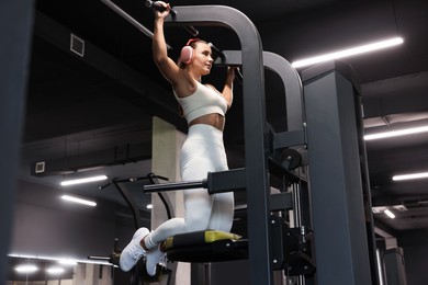Photo of Athletic woman in headphones training on pull up machine in gym, low angle view