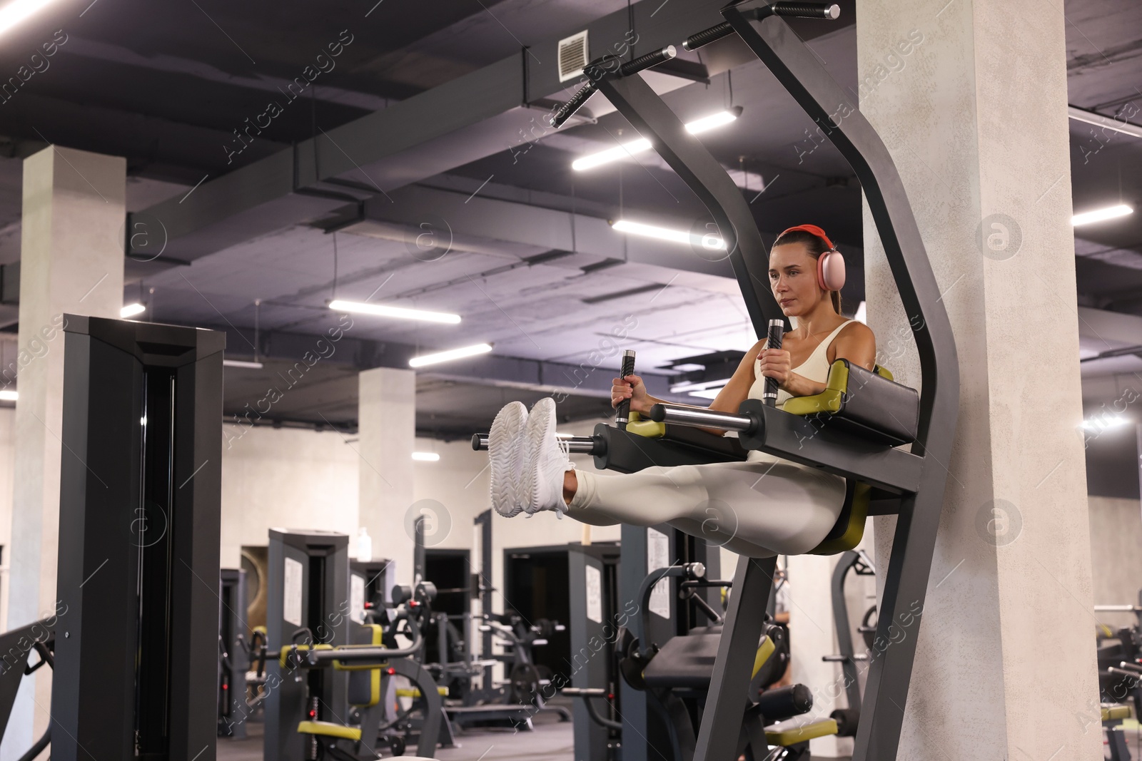Photo of Athletic woman in headphones training on power tower in gym. Space for text