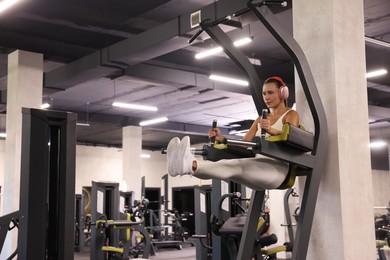 Photo of Athletic woman in headphones training on power tower in gym. Space for text