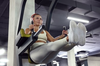 Photo of Athletic woman in headphones training on power tower in gym, low angle view