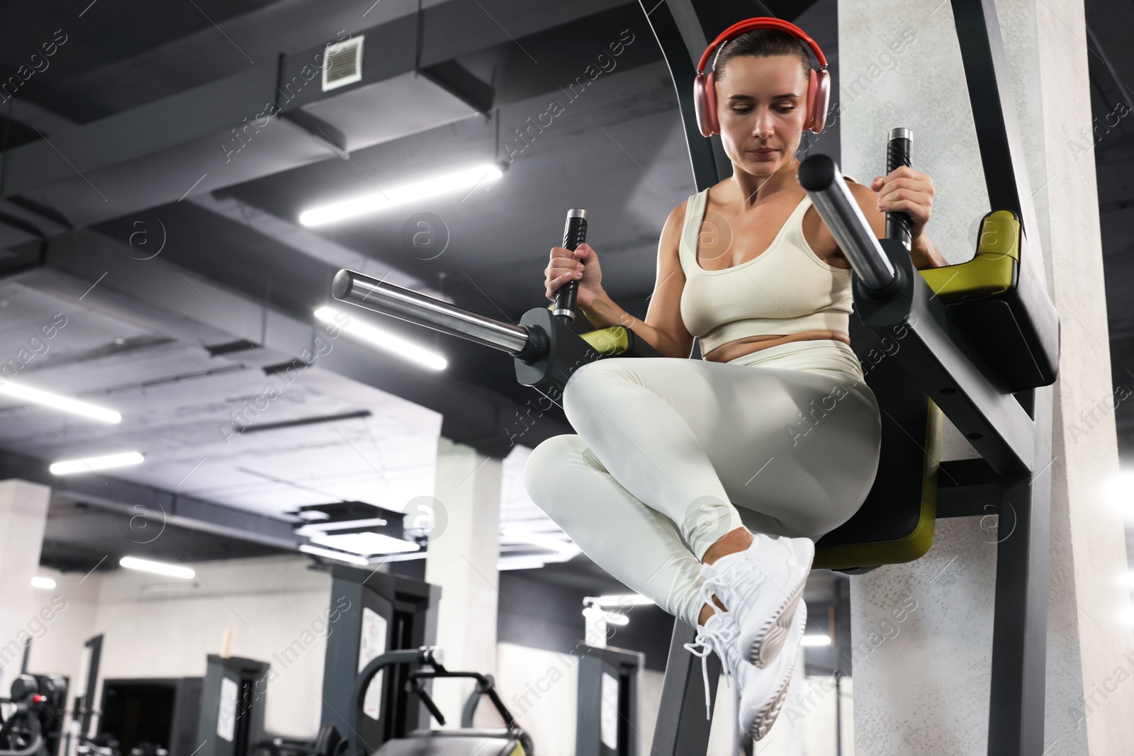 Photo of Athletic woman in headphones training on power tower in gym, low angle view. Space for text