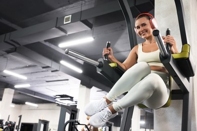 Photo of Smiling woman in headphones training on power tower in gym, low angle view. Space for text