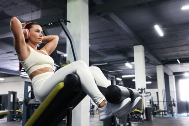 Photo of Athletic woman in headphones training on exercise bench in gym. Space for text