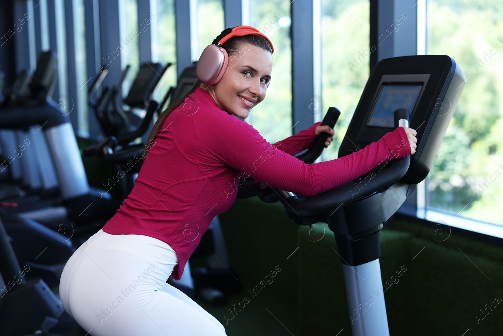Photo of Smiling woman in headphones training on exercise bike in gym