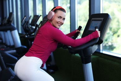 Photo of Smiling woman in headphones training on exercise bike in gym