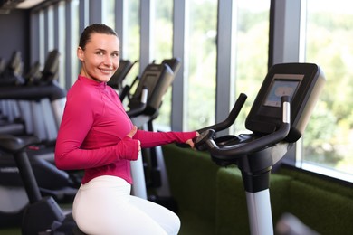 Photo of Smiling woman showing thumbs up on exercise bike in gym