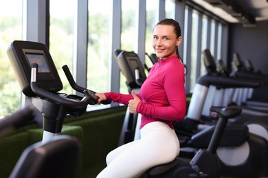 Photo of Smiling woman showing thumbs up on exercise bike in gym