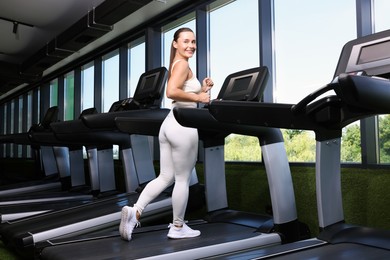 Photo of Smiling woman training on treadmill in gym, low angle view