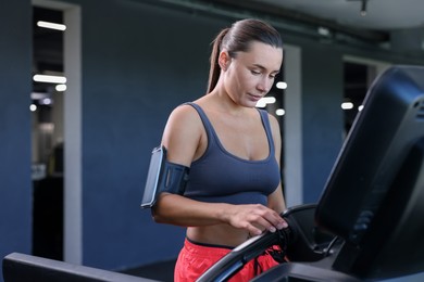 Photo of Athletic woman with armband training on treadmill in gym