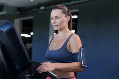 Photo of Athletic woman with armband training on treadmill in gym