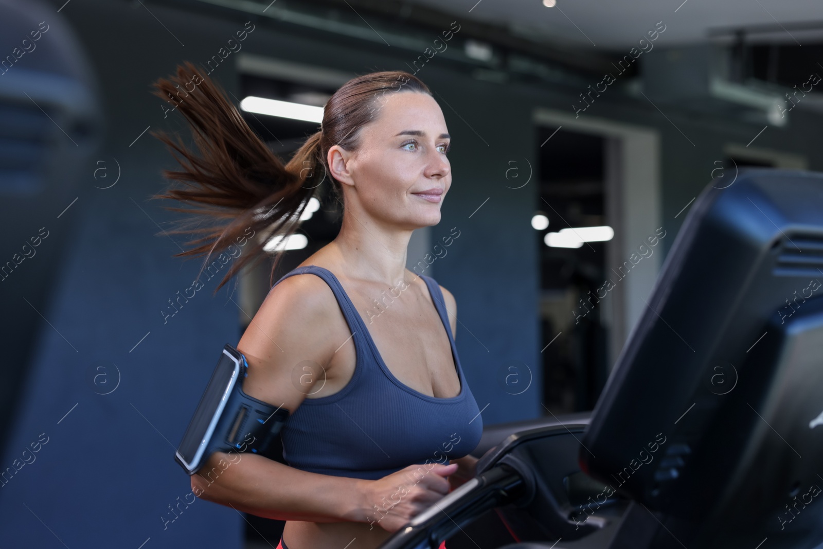 Athletic woman with armband training on treadmill in gym Photo of Athletic woman with armband training on treadmill in gym