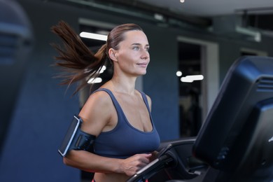 Photo of Athletic woman with armband training on treadmill in gym