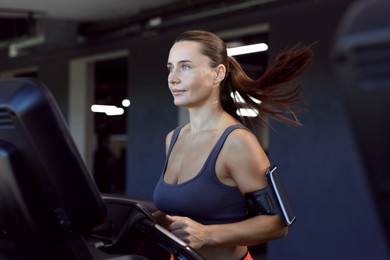 Photo of Athletic woman with armband training on treadmill in gym