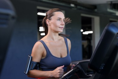 Photo of Athletic woman with armband training on treadmill in gym