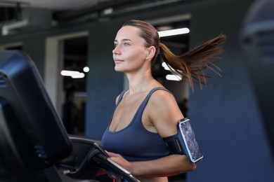 Photo of Athletic woman with armband training on treadmill in gym