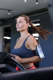Photo of Athletic woman with armband training on treadmill in gym