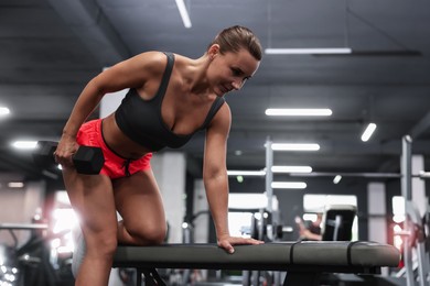 Photo of Athletic woman training with dumbbell on exercise bench in gym, low angle view