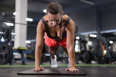 Photo of Athletic woman doing plank exercise on yoga mat in gym