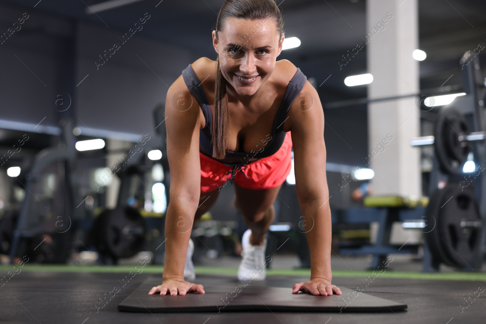 Smiling woman doing plank exercise on yoga mat in gym Photo of Smiling woman doing plank exercise on yoga mat in gym