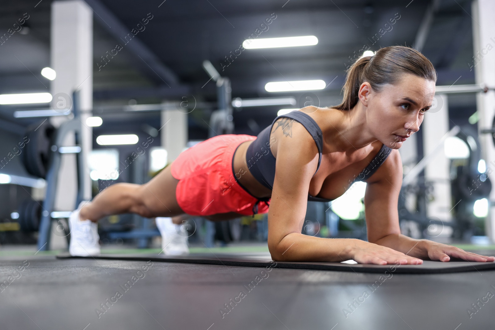 Athletic woman doing plank exercise on yoga mat in gym Photo of Athletic woman doing plank exercise on yoga mat in gym