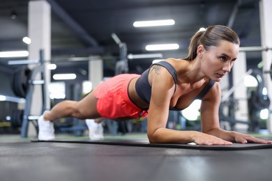 Photo of Athletic woman doing plank exercise on yoga mat in gym