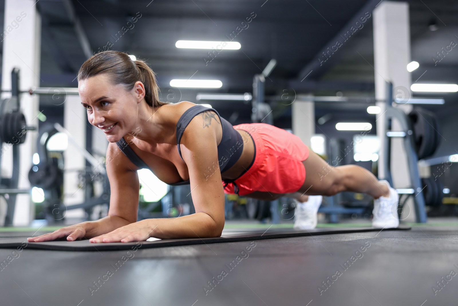Smiling woman doing plank exercise on yoga mat in gym Photo of Smiling woman doing plank exercise on yoga mat in gym